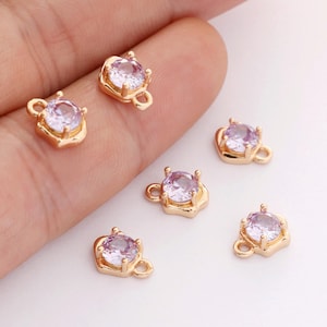 May include: Six gold-tone heart-shaped charms with a clear round purple rhinestone in the centre. Each charm has a loop for attaching to jewellery.
