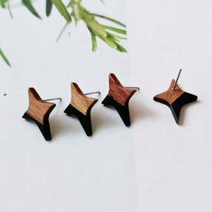 May include: A pair of wooden star-shaped earrings with black paint on the bottom half of each star. The earrings are on a white surface.
