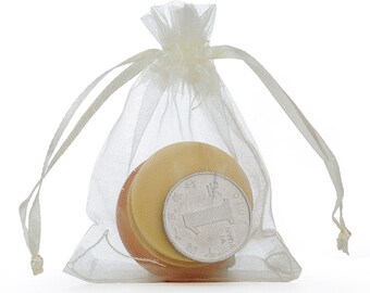 Puede incluir: Una bolsa de organza blanca transparente con cierre de cordón, que contiene un objeto redondo multicolor y una moneda china plateada con el número "1" en ella.