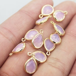 Puede incluir: Un grupo de diez abalorios de forma de lágrima de color dorado con un inserto de vidrio de color lavanda pálido. Cada abalorio tiene un bucle en la parte superior para sujetarlo a joyas.