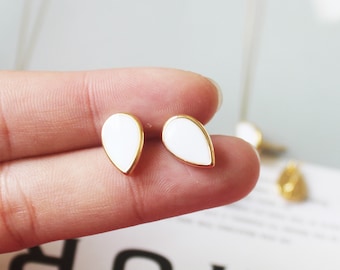 May include: A pair of gold teardrop earrings with white enamel. The earrings are small and delicate.