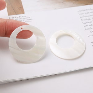 May include: Two white shell hoop earrings with a smooth, iridescent finish. The earrings are approximately 2 inches in diameter.
