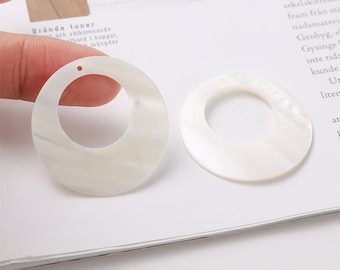 May include: Two white shell hoop earrings with a smooth, iridescent finish. The earrings are approximately 2 inches in diameter.