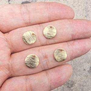 Peut inclure: Quatre petits charms ronds en métal doré avec une finition brossée texturée. Chaque charm a un petit trou en haut pour l'enfilage. Ces charms sont idéaux pour la fabrication de bijoux ou d'autres projets d'artisanat.