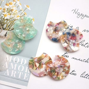 May include: Four pairs of colorful, semi-circular resin earrings. The earrings are made of a translucent material with a marbled pattern. The colors include green, pink, blue, and white.