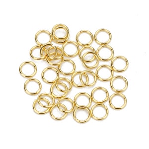 May include: A pile of gold jump rings, a type of jewelry finding used for connecting chains, cords, and other jewelry components.