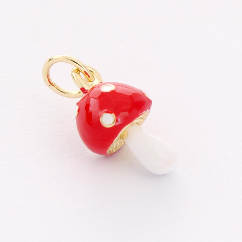 May include: A gold charm in the shape of a red mushroom with white spots. The mushroom has a white stem.