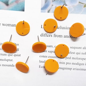 May include: A set of eight orange round earring blanks with a hole in the center. The earring blanks are made of plastic and have a shiny finish.
