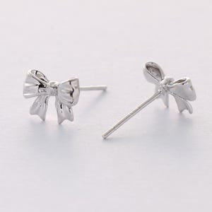 May include: A pair of silver bow-shaped stud earrings.