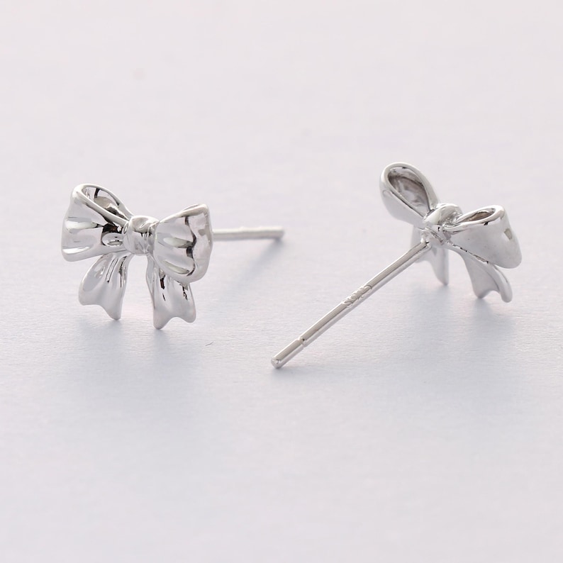 May include: A pair of silver bow-shaped stud earrings.