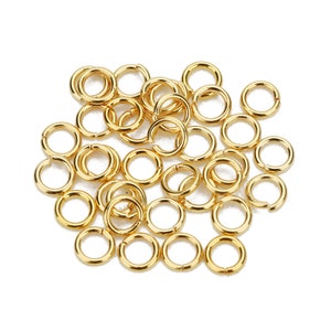 May include: A pile of gold jump rings, a type of jewelry finding used for connecting chains, cords, and other jewelry components.
