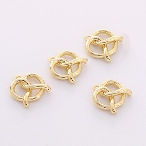 May include: Four gold-colored metal charms shaped like pretzels. The charms have a loop at the top for attaching to jewelry or other crafts.