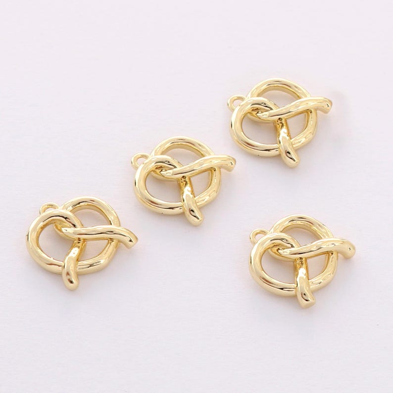 May include: Four gold-colored metal charms shaped like pretzels. The charms have a loop at the top for attaching to jewelry or other crafts.