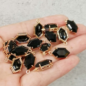 May include: A collection of black gemstone pendants with gold-colored metal frames. The pendants have various geometric shapes, including hexagons and elongated octagons. Each pendant has a small loop for attaching to a chain or other jewelry component.