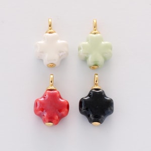 May include: Four ceramic cross-shaped pendants in white, light green, red, and black. Each pendant has a gold-colored bail and a gold-colored bead at the bottom. The pendants are arranged on a white background.