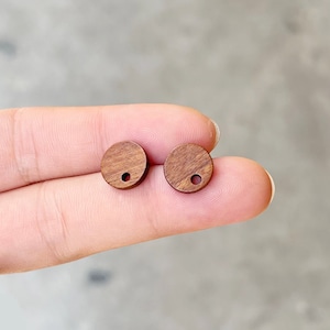 May include: Two round wooden earrings with a small hole in the center. The earrings are a dark brown color.