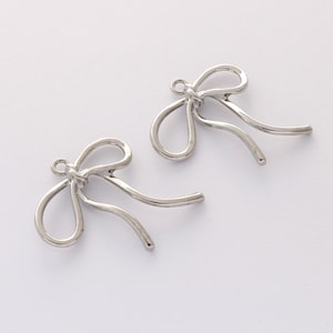 Op de afbeelding: Twee zilveren metalen strikbedels met een lus aan de bovenkant om te bevestigen aan sieraden of andere knutselwerkjes.