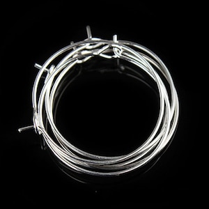 May include: A set of silver hoop earrings, stacked on top of each other. The hoops are thin and delicate, and they are perfect for everyday wear.