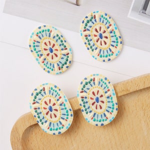 May include: Four oval-shaped ceramic tiles with a white background and a colorful mosaic design. The design features a central flower with blue, red, yellow, and green accents.