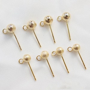 May include: Eight gold-toned earring posts with textured ball tops. The posts are straight and have a loop at the top for attaching to earrings.