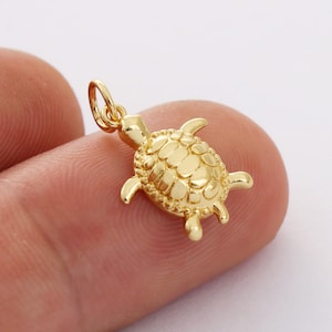 Puede incluir: Un colgante de tortuga de color dorado. La tortuga está detallada con un caparazón texturizado y tiene un bucle en la parte superior para sujetarlo a una cadena o pulsera.