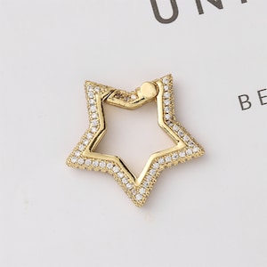May include: Gold-toned star-shaped charm with clear rhinestones around the perimeter. The charm has a small opening at the top for attaching to a necklace or bracelet.