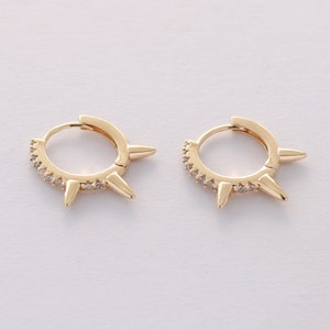 May include: Gold hoop earrings with small spikes and clear cubic zirconia stones.