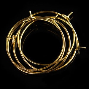 May include: A set of five gold hoop earrings, stacked on top of each other. The hoops are all the same size and have a simple, classic design.