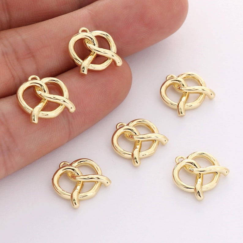 May include: Six gold-colored metal pretzel charms. The charms are shaped like pretzels and have a loop at the top for attaching to a necklace or bracelet.