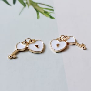 May include: Two gold-tone heart-shaped charms with white enamel. One charm is a padlock with a keyhole and the other is a key. The charms are attached to a gold-tone chain.