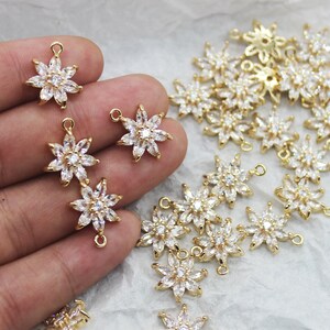 Puede incluir: Un grupo de abalorios en forma de flor de metal dorado con detalles de cristal transparente. Los abalorios tienen un bucle en la parte superior y un pequeño bucle en la parte inferior para sujetarlos a joyas.