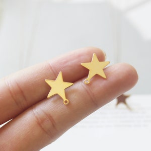 May include: Two gold-coloured star-shaped charms with a small hole at the bottom. The charms are on a finger.