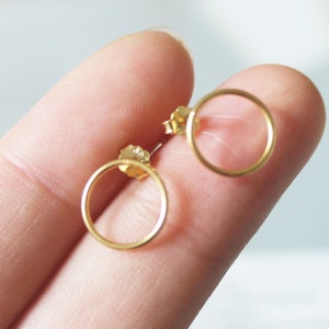 May include: A pair of gold-toned circle stud earrings. The earrings are small and delicate, and they are perfect for everyday wear.