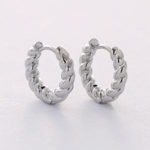 May include: A pair of silver hoop earrings with a twisted design.