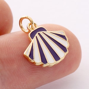 May include: A gold-colored seashell charm with a white and navy blue enamel design. The charm has a gold-colored loop at the top for attaching to a necklace or bracelet. The seashell design is detailed and has a glossy finish.