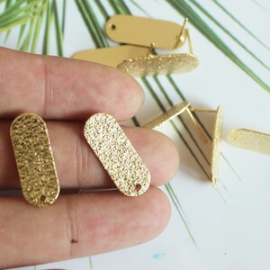 May include: Gold-toned metal oval earring blanks with a textured surface. The blanks have a small hole at the top for attaching earring findings.