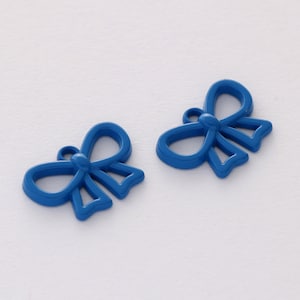 Pode incluir: Dois pingentes de metal azul em forma de laço com um furo para pendurar. Os laços são de design simples e forma arredondada.