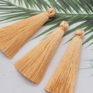 May include: Three peach-coloured fabric tassels with a knotted top. The tassels are made of soft, silky threads and are approximately 7.6 cm long.