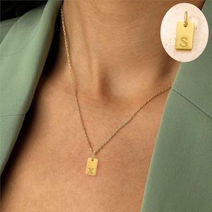 May include: A gold chain necklace with a small rectangular pendant featuring the letter "X" engraved on it.