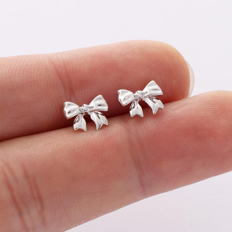 May include: A pair of silver bow-shaped stud earrings.