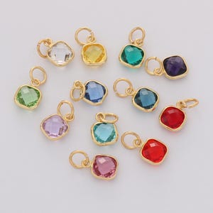 May include: A collection of gold-colored pendants with various colored square-cut gemstones. The gemstones include clear, yellow, green, purple, blue, red, and pink. Each pendant has a small loop for attaching to a chain or bracelet.