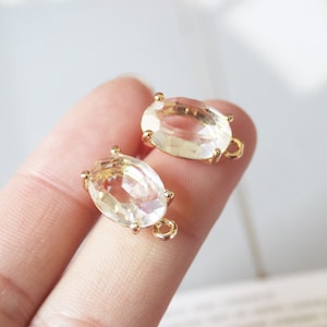 Puede incluir: Dos abalorios ovalados de cristal en tono dorado con un bucle para sujetar a las joyas. Los cristales son transparentes y tienen un diseño facetado.