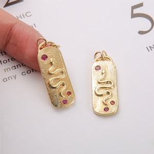 May include: Two gold-tone pendant charms featuring a snake design and red rhinestones. The charms are rectangular and have a textured surface.