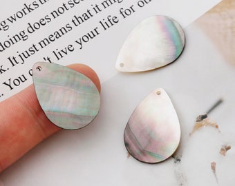 May include: Three iridescent white teardrop-shaped shell pendants with a hole at the top for stringing. The shells have a pearlescent finish and a subtle green and pink hue.