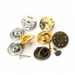 May include: A set of 10 metal pin backs in three finishes: silver, gold, and antique brass. Each pin back has a round base with a small pin and a locking clasp.