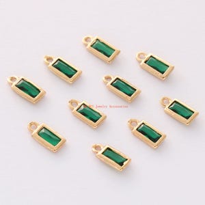 May include: Ten gold-toned rectangular charms with emerald green glass stones. Each charm has a loop at the top for attaching to jewelry.