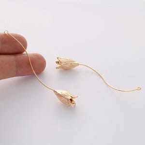 Può includere: Un paio di orecchini dorati con un delicato design floreale. Gli orecchini sono realizzati in filo sottile e hanno un piccolo ciondolo a forma di fiore all'estremità.