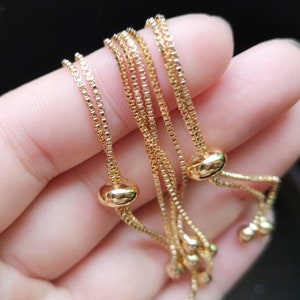 May include: A set of three gold chain bracelets with adjustable sliding knots. Each bracelet has a small round bead at the end of the knot.