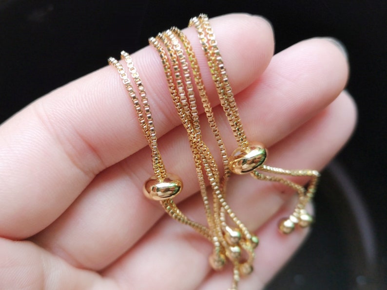 May include: A set of three gold chain bracelets with adjustable sliding knots. Each bracelet has a small round bead at the end of the knot.