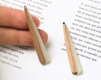 Puede incluir: Dos colgantes en forma de lágrima de madera y resina blanca. Cada colgante tiene un pequeño agujero en la parte superior para ensartar. La veta de la madera es visible en la mitad superior de los colgantes.